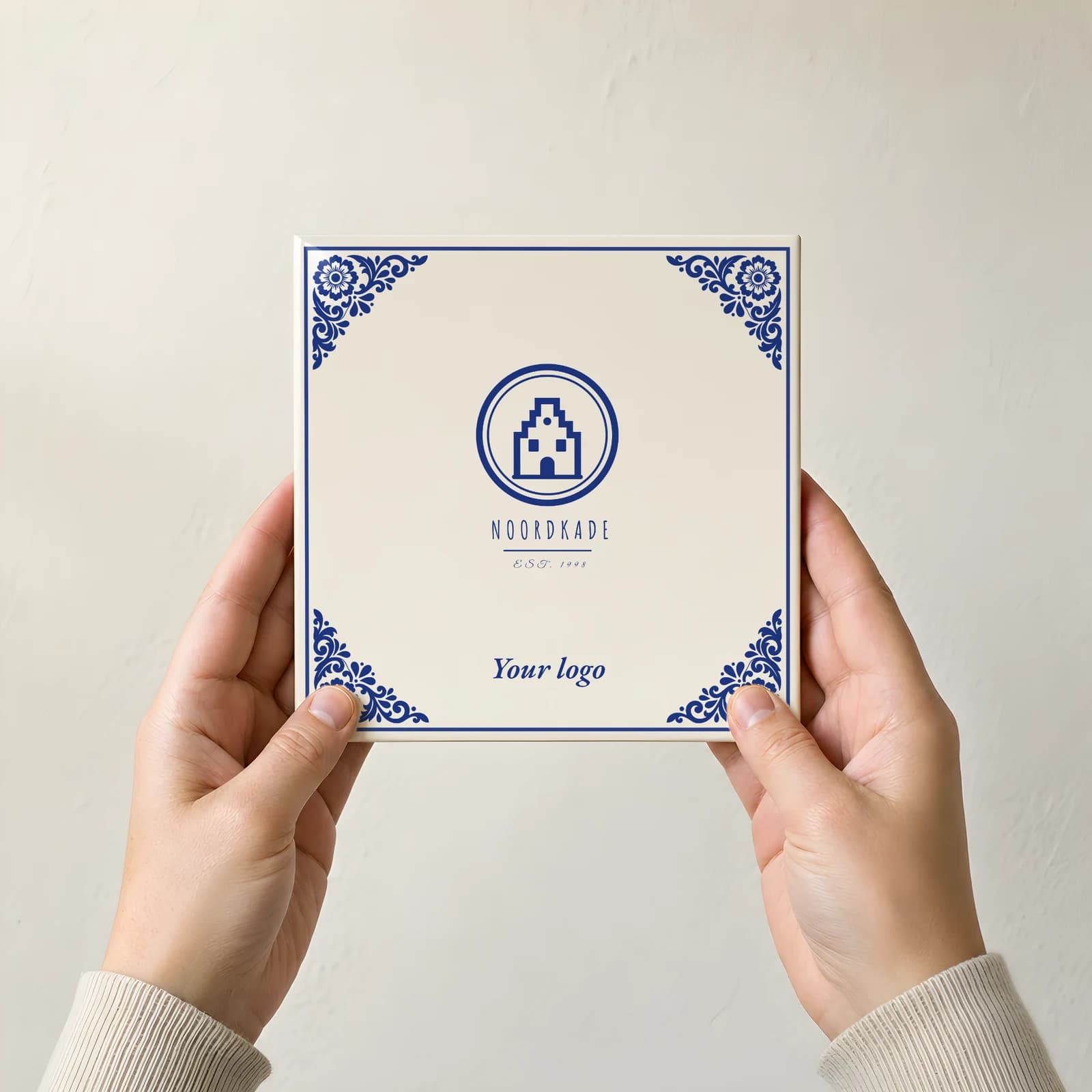 Two hands holding a Delft Blue logo tile